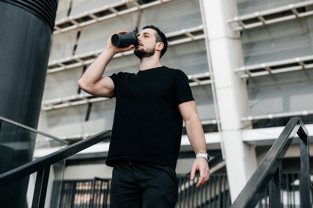 Tempo di idratazione! Uomo che beve acqua dalla bottiglia sportiva dopo aver fatto jogging. Duro lavoro. Abbi cura di te concetto. Bevi più acqua. Non dimenticare di bere durante l'allenamento.