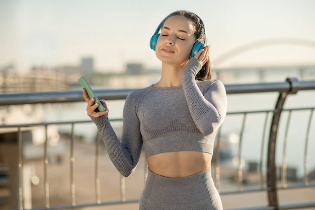 Tempo di musica. Ragazza in forma in abiti sportivi grigi che ascolta musica e sembra premurosa