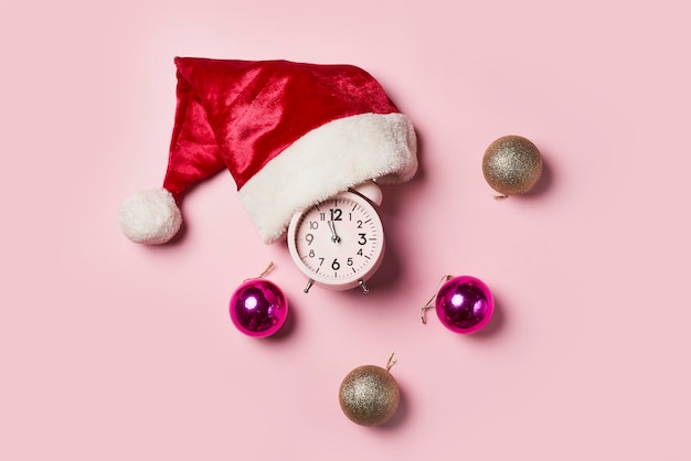 Tempo di Nataleorologio di Natale con un cappello di Babbo Natale o un berretto e palle di Natale su uno sfondo rosa t