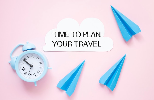 Tempo di pianificare il tuo viaggio testo su carta con orologio e aeroplano di carta su un tavolo rosa.