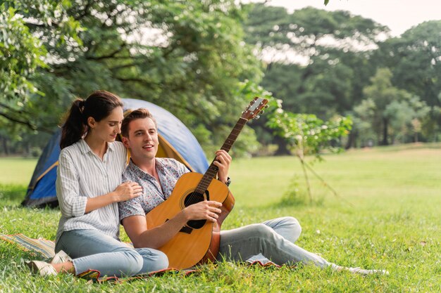 Tempo di picnic e campeggio. Giovani coppie divertendosi con la chitarra sul picnic e accampandosi nel parco.