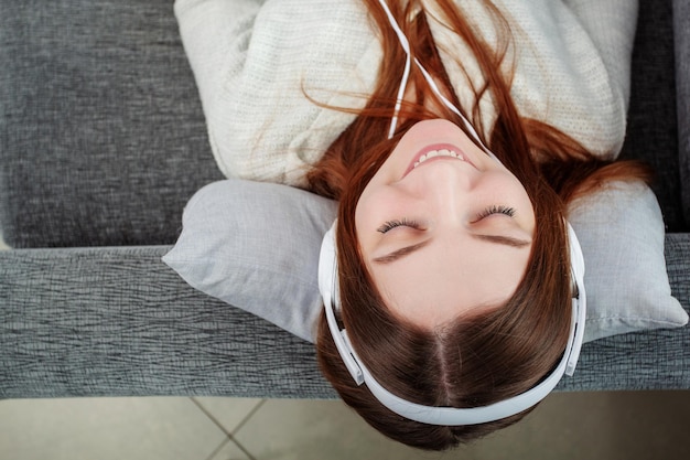 Tempo di relax sul divano bella ragazza sorridente sdraiata sul divano e ascoltando la musica con