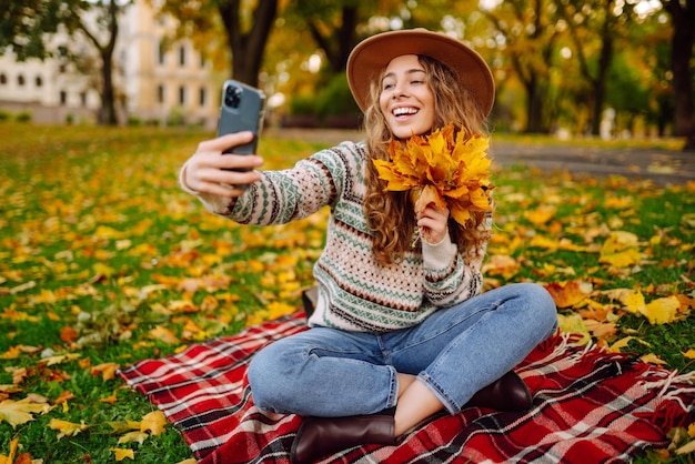 Tempo di selfie Bella donna prende selfie sullo smartphone con cappello sul prato nel parco autunnale su plaid