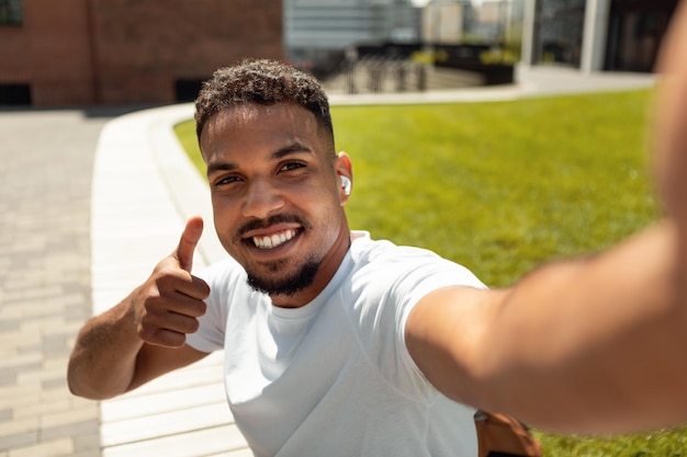 Tempo di selfie felice uomo afroamericano che fa foto di lui e mostra il pollice in su mentre cammina dentro