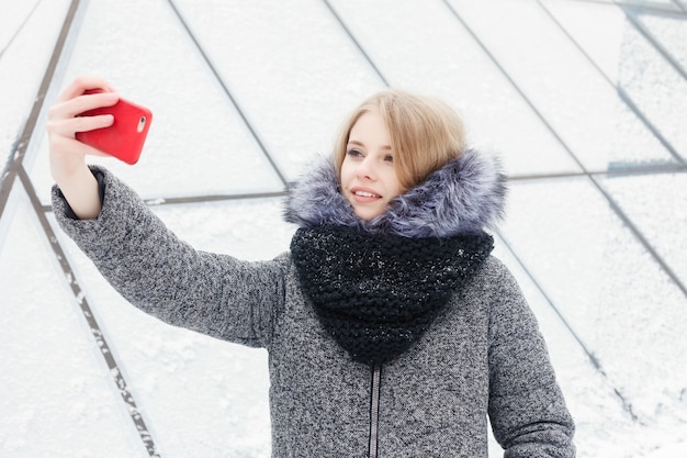 Tempo di selfie, giovane blogger funky sta facendo foto per la sua pagina sui social network. Giovane donna felice che prende selfie. Tempo soleggiato freddo. Concetto di inverno della donna.