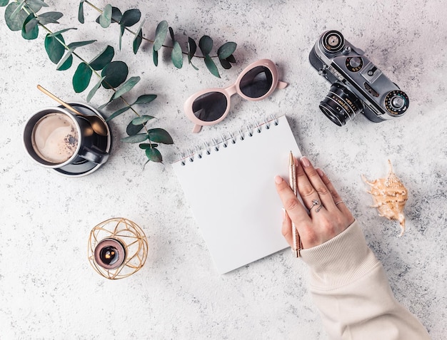 Tempo di viaggiare e concetto di voglia di viaggiare La ragazza del viaggiatore hipster tiene la penna Fotocamera occhiali da sole taccuino candela e tazza di caffè su sfondo bianco Donna che pianifica le vacanze estive Vista dall'alto piatto