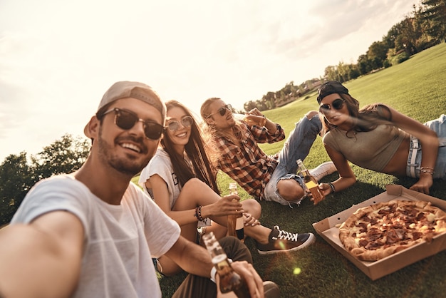 Tempo di vita! Autoritratto di giovani in abbigliamento casual che sorridono mentre si gustano pizza e birra all'aperto