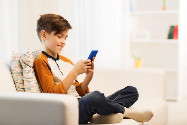 tempo libero, bambini, tecnologia, comunicazione internet e concetto di persone - ragazzo sorridente con messaggio di testo sullo smartphone o gioco a casa