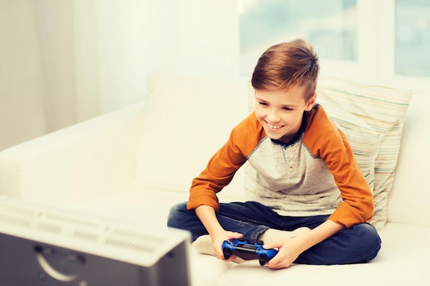 tempo libero, bambini, tecnologia e concetto di persone - ragazzo sorridente con joystick che gioca a videogiochi a casa