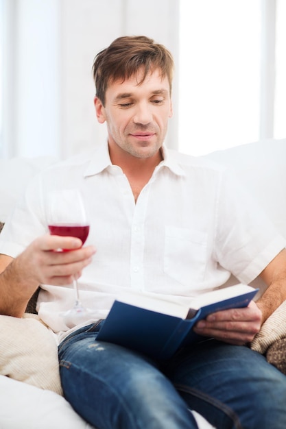 tempo libero, bevande, pensione, istruzione e concetto di stile di vita - uomo felice con libro e bicchiere di vino rosato a casa