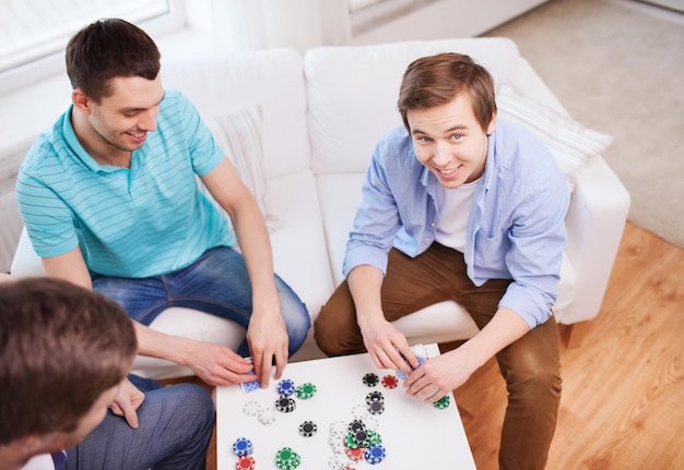 tempo libero, giochi, amicizia, gioco d'azzardo e intrattenimento: tre amici maschi sorridenti che giocano a carte a casa