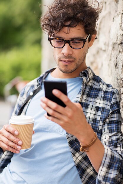 tempo libero, tecnologia, comunicazione e concetto di persone - uomo con smartphone che beve caffè da una tazza di carta usa e getta e messaggio di testo sulla strada della città