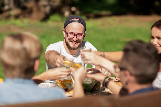 tempo libero, vacanze, mangiare, persone e concetto di cibo - amici felici che tintinnano i bicchieri e festeggiano alla festa estiva in giardino