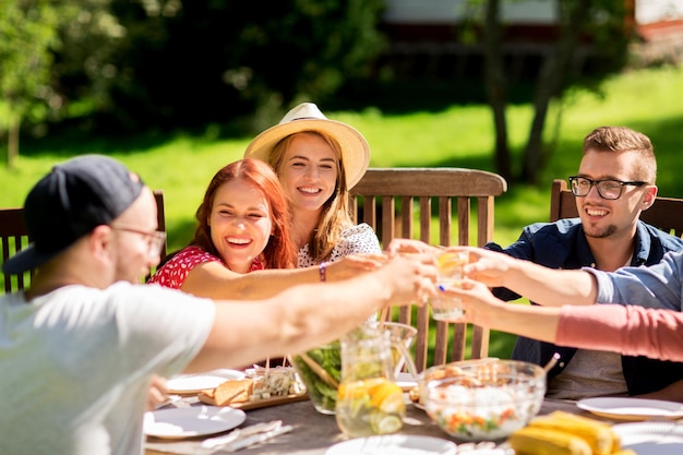 tempo libero, vacanze, mangiare, persone e concetto di cibo - amici felici che tintinnano i bicchieri e festeggiano alla festa estiva in giardino