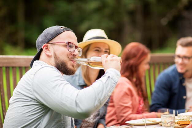 tempo libero, vacanze, mangiare, persone e concetto di cibo - uomo felice che beve birra dalla bottiglia a cena con gli amici alla festa estiva in giardino