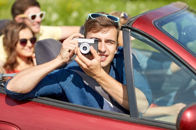 tempo libero, viaggio su strada, viaggi, vacanze estive e concetto di persone - amici felici che guidano in auto cabriolet e scattano foto con la cinepresa