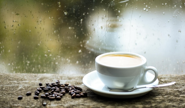 Tempo nuvoloso autunnale migliore con bevanda alla caffeina Gustare il caffè nei giorni di pioggia Caffè appena preparato Tazza bianca e fagioli sul davanzale Finestra di vetro bagnata e tazza di caffè caldo Rituale del caffè mattutino