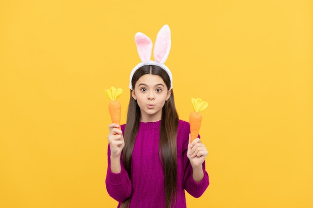 tempo per divertirsi. bellissimo bambino che indossa divertenti orecchie di lepre. vacanze di Pasqua primaverili. la ragazza teenager stupita indossa le orecchie da coniglio tengono la carota. Buona Pasqua. felicità dell'infanzia. bambino in costume da coniglio.