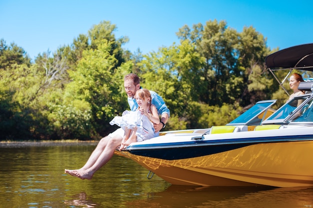 Tempo prezioso insieme. Il giovane padre ottimista e la sua piccola figlia seduti sulla prua della barca e osservano i pesci nell'acqua del fiume