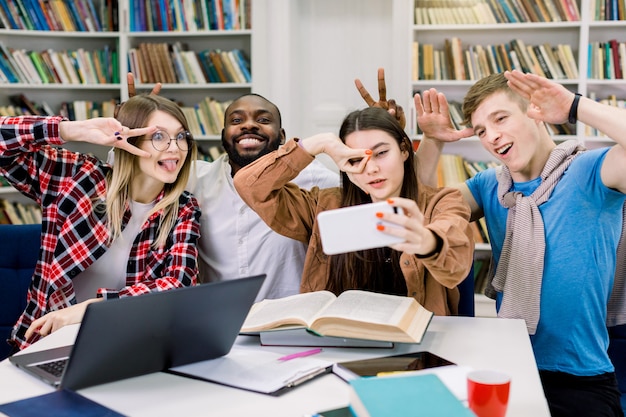 Tempo selfie in biblioteca. Quattro studenti internazionali allegri, intelligenti e di successo