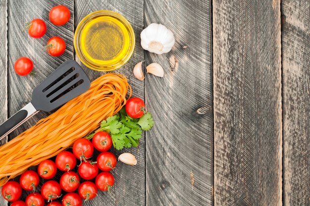 Tenaglie di pomodori ciliegia, pasta, olio d'oliva, aglio, erbe e pasta sullo sfondo in legno vecchio. Stile rustico. Cibo italiano tradizionale.