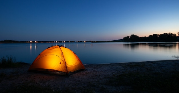 Tenda illuminata interna arancione su un lago al crepuscolo