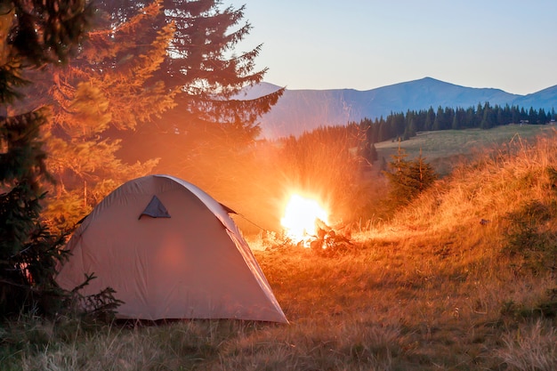 Tenda per escursionisti in montagna alla sera con un falò con scintillii vicino