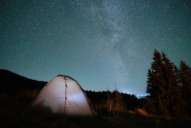 Tenda turistica illuminata e luminosa sul campeggio in montagne scure sotto il cielo notturno con stelle scintillanti Concetto di stile di vita attivo