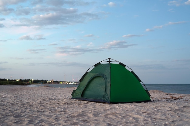 Tenda verde sulla riva sabbiosa contro il cielo blu e lo sfondo del mare Campeggio turismo attivo