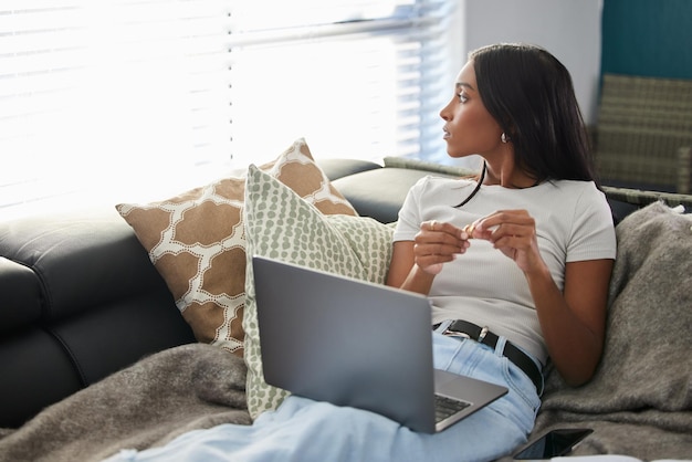 Tendo sempre a isolarmi quando sono a casa Inquadratura di una giovane donna attraente seduta da sola sul divano e con aria contemplativa mentre usa il suo laptop