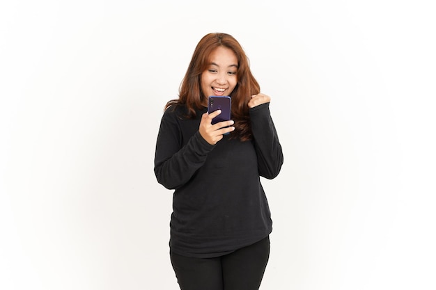 Tenendo e utilizzando lo smartphone di una bella donna asiatica che indossa una camicia nera isolata su bianco