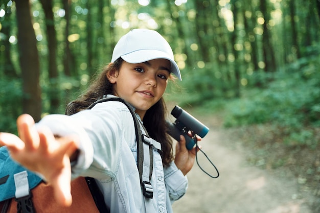 Tenendo il binocolo La ragazza è nella foresta durante il giorno d'estate alla scoperta di nuovi posti