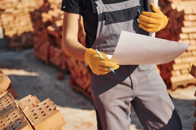 Tenendo il piano nelle mani Operaio edile in uniforme e equipaggiamento di sicurezza ha un lavoro sulla costruzione