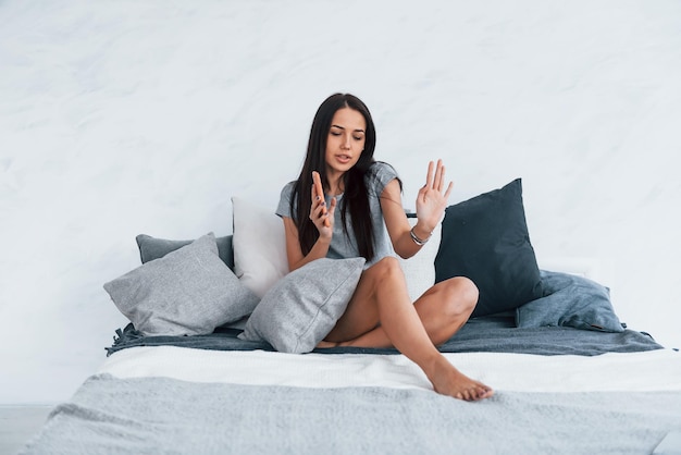 Tenendo il telefono in mano e ascolta la musica con le cuffie wireless. Giovane bella donna in abiti casual seduto a casa da solo sul letto.