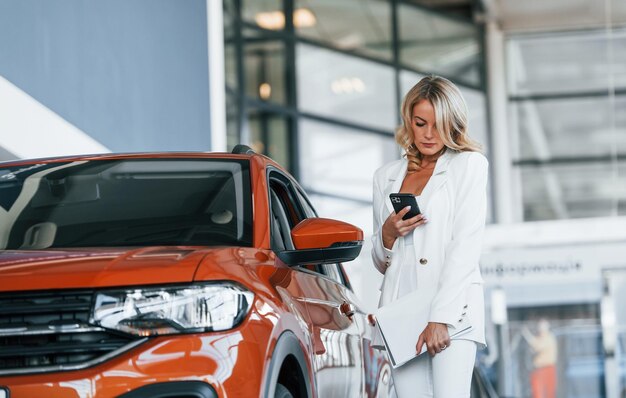 Tenendo il telefono Una donna in abiti formali è al chiuso nell'autosalone