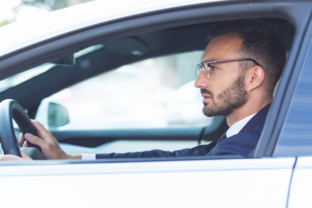 Tenendo il volante. Uomo barbuto che indossa un abito scuro che tiene il volante mentre guida l'auto