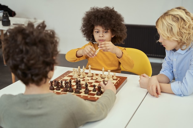 Tenendo in mano un pezzo fantastico ragazzini che discutono del gioco mentre sono seduti al tavolo e giocano a scacchi