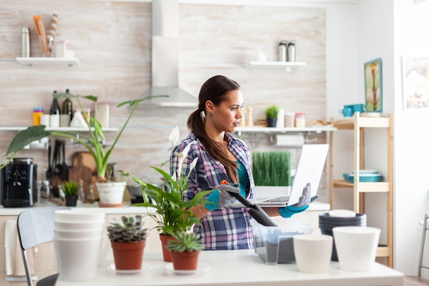 Tenendo la pala per il giardinaggio e il laptop in cucina in cerca di decorazioni per la casa