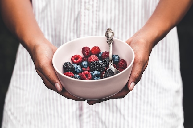 Tenendo un piatto pieno di frutti di bosco. Mix per la colazione. Lamponi, mirtilli, more. piatto