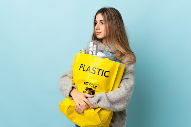 Tenendo un sacchetto pieno di bottiglie di plastica da riciclare sul lato dall'aspetto blu isolato