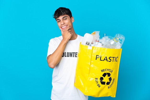 Tenendo una borsa piena di bottiglie di plastica da riciclare sul muro blu felice e sorridente