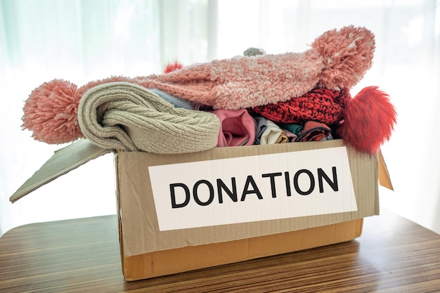 Tenendo una scatola per la donazione di vestiti con vestiti usati e bambola a casa per sostenere l'aiuto per i poveri nel mondo.