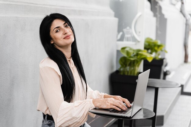 Tenera donna con mani da vitiligine e laptop in caffetteria all'aperto Mani con pigmentazione cutanea da vitiligine Stile di vita con malattie stagionali della pelle Lavoro a distanza online con laptop