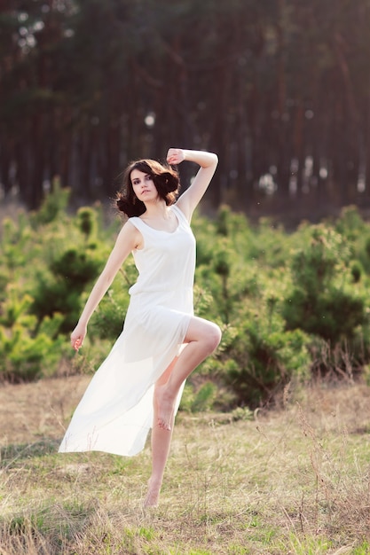 Tenera donna in abito bianco ballando sulla natura