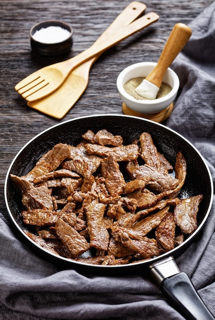 Tenera e succosa bistecca di manzo fritta ribeye tagliata a strisce, bistecca minuto su una padella su un tavolo di legno scuro, vista verticale dall'alto