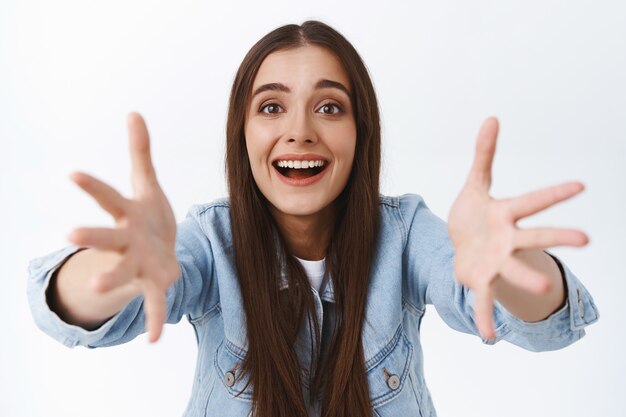 Tenera, femminile, bella donna bruna in giacca di jeans, sorridente sospirando di ammirazione e affetto, ansimando stupita, guarda qualcosa di prezioso e meraviglioso, vuole tenere qualcosa o abbracciare