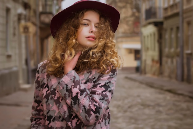 Tenera modella bionda con cappello e cappotto rossi per strada