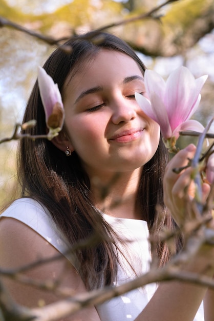 Tenera ragazza con gli occhi chiusi in fiori di magnolia Primo piano del viso