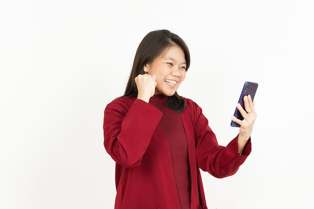 Tenere e utilizzare lo smartphone di una bella donna asiatica che indossa una camicia rossa isolata su sfondo bianco