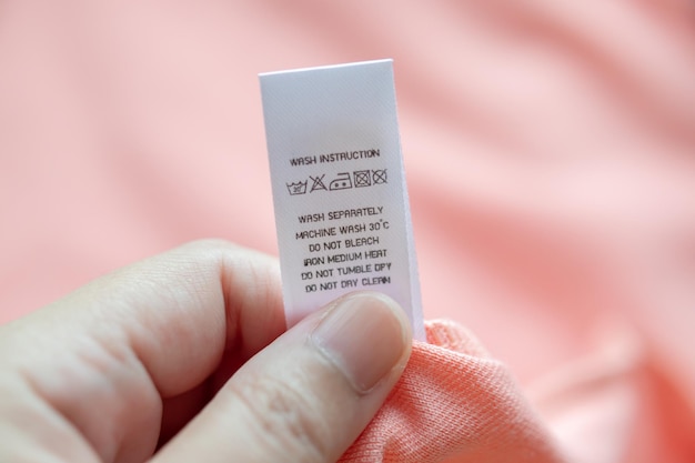 Tenere in mano e leggere al bucato bianco istruzioni per il lavaggio etichetta dei vestiti sulla camicia rosa